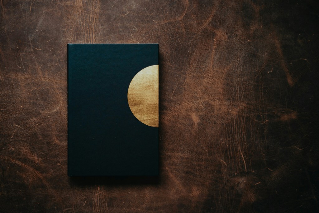 Minimal dark astrology journal with gold crescent moon detail on textured wooden surface
