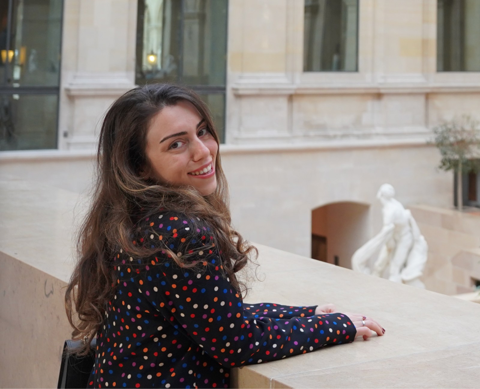 Simge, founder of Simgology, smiling beside a stone balustrade at the Louvre